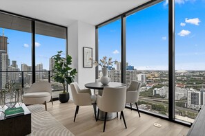 A modern living room with a city view, a round dining table, and comfortable seating. - 26th Floor E11EVEN Retreat with Skyline & Bay Views (Miami)