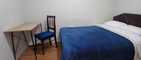 A bedroom with a bed, a desk, and a chair.