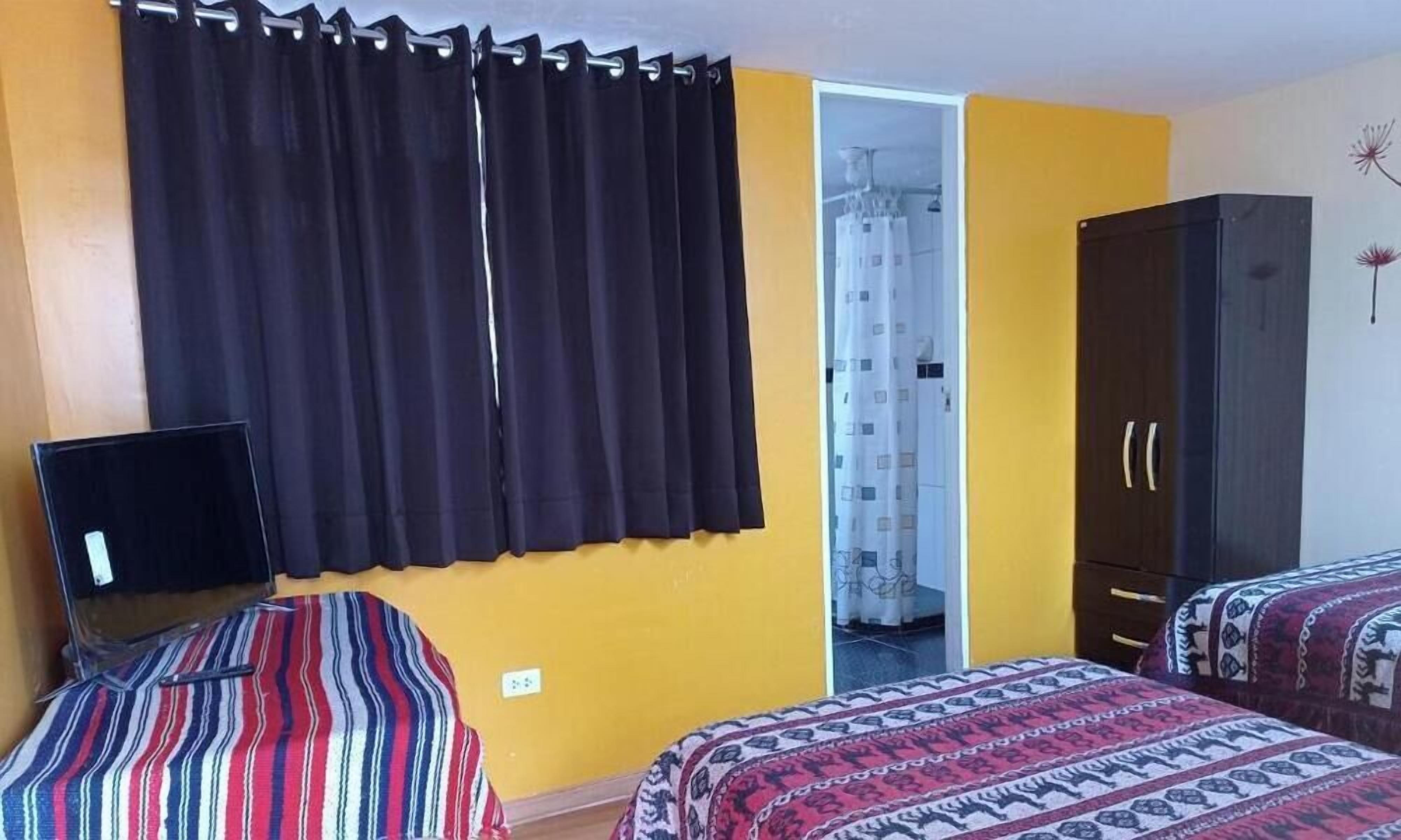 A room with two beds, a wardrobe, a desk with a computer, and a curtain.