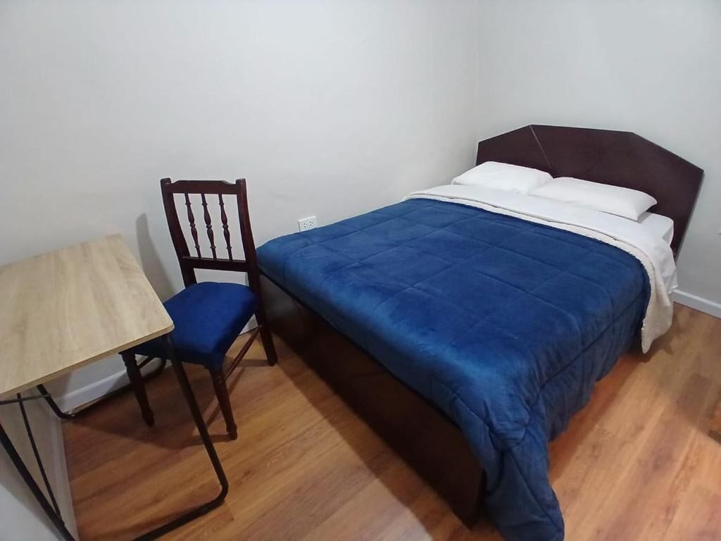 Un dormitorio con una cama, una silla de madera y una mesita.