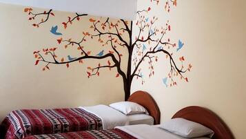 Un dormitorio con dos camas, un mural en la pared con un árbol, hojas y pájaros, y una pared lisa.