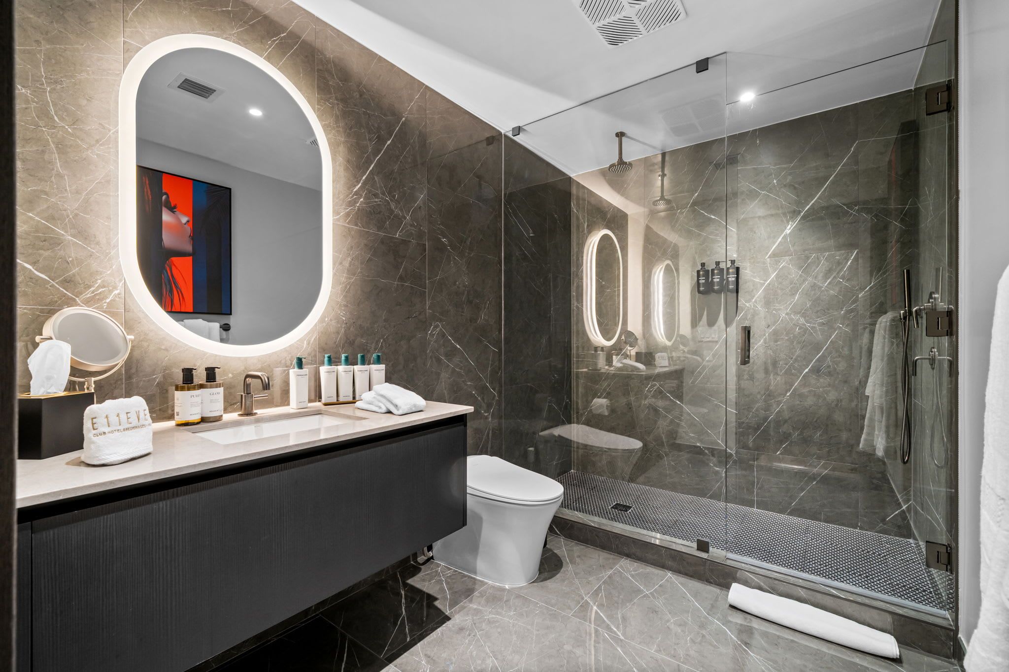 Un bagno moderno con parete in marmo, uno specchio rotondo, un WC e una cabina doccia in vetro.