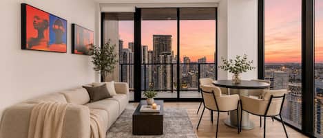 Ein modernes Wohnzimmer mit Sofa, Couchtisch und Sesseln, Blick auf die Stadt durch große Fenster sowie Kunstwerken an der Wand.