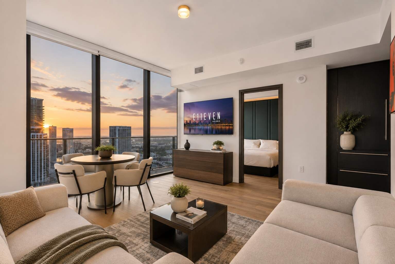 A modern living room with a city view, a dining area, and a bedroom with a bed and nightstand.