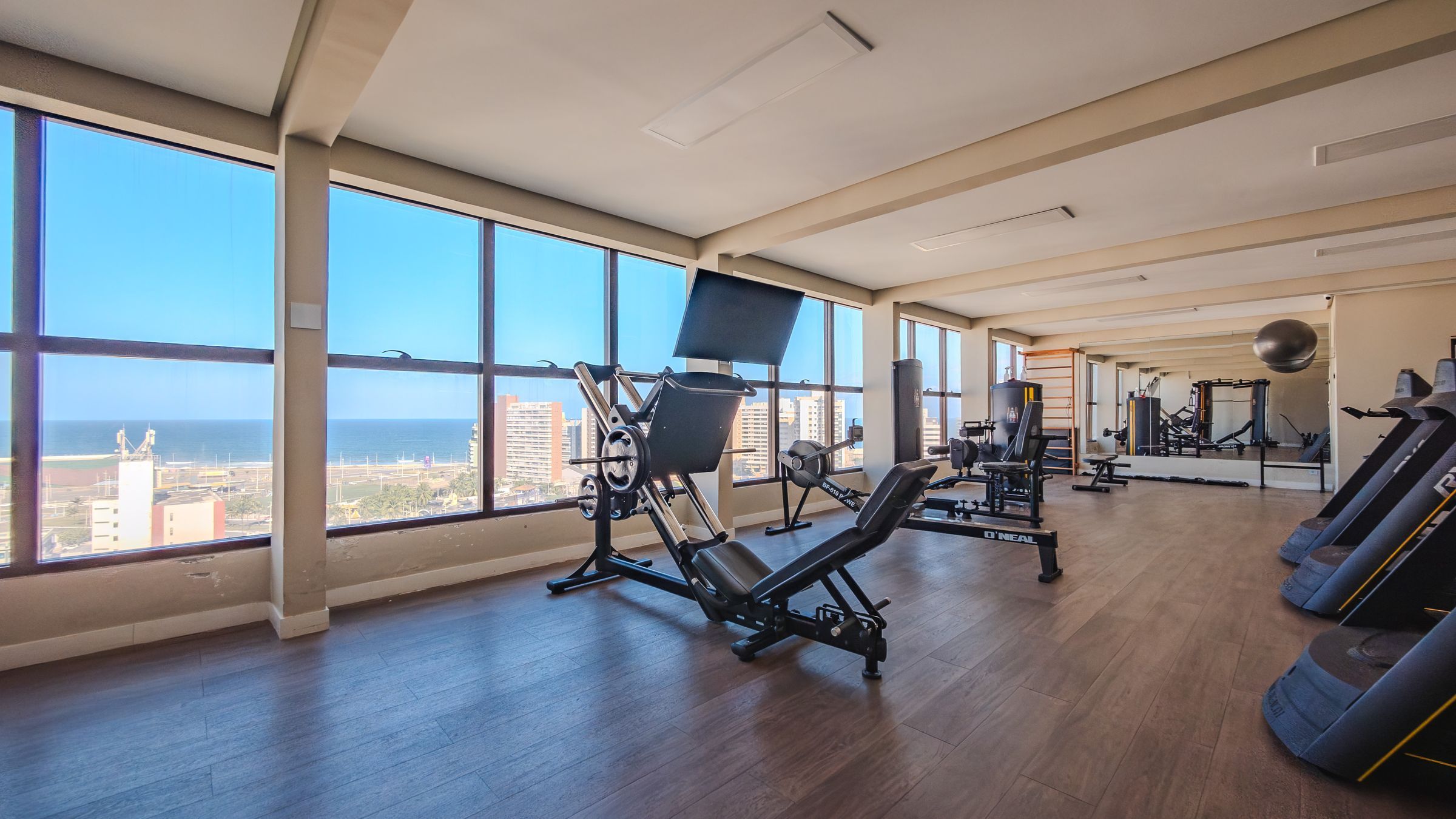 A gym with exercise equipment, large windows, and a view of the city.