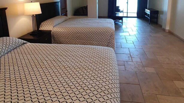 Une chambre d’hôtel avec deux lits, une table de chevet, une lampe, un bureau et une chaise.