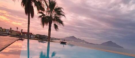 Ein Swimmingpool mit klarem Wasser, das Palmen und einen Sonnenuntergang reflektiert.