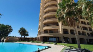 Un hôtel à plusieurs étages doté d’une piscine, de palmiers et surplombant un ciel d’un bleu éclatant.
