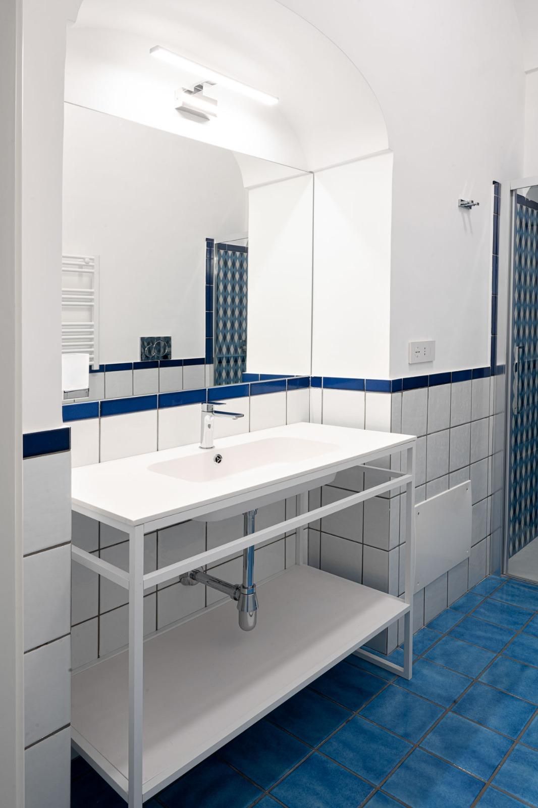 Un baño con un lavamanos blanco, piso con azulejos azules y un espejo grande.