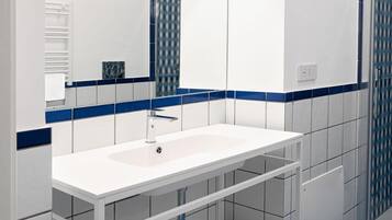 Un baño con un lavamanos blanco, piso con azulejos azules y un espejo grande.