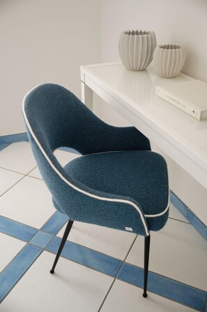 Une chaise recouverte d’un tissu foncé, dotée d’une structure en métal, placée sur un sol carrelé de carreaux bleus et blancs.