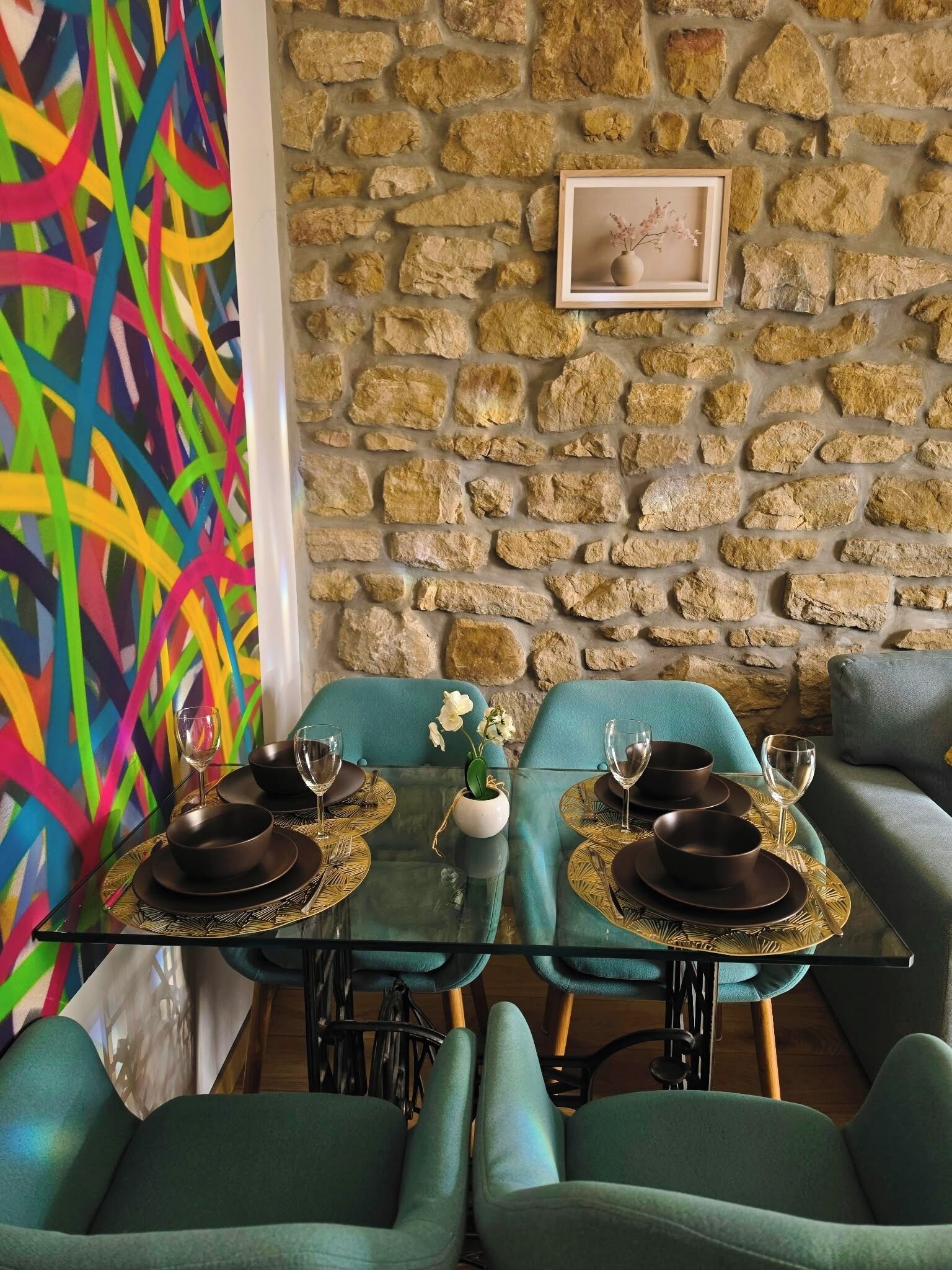Un comedor con pared de piedra, un cuadro abstracto de colores y sillas color turquesa.