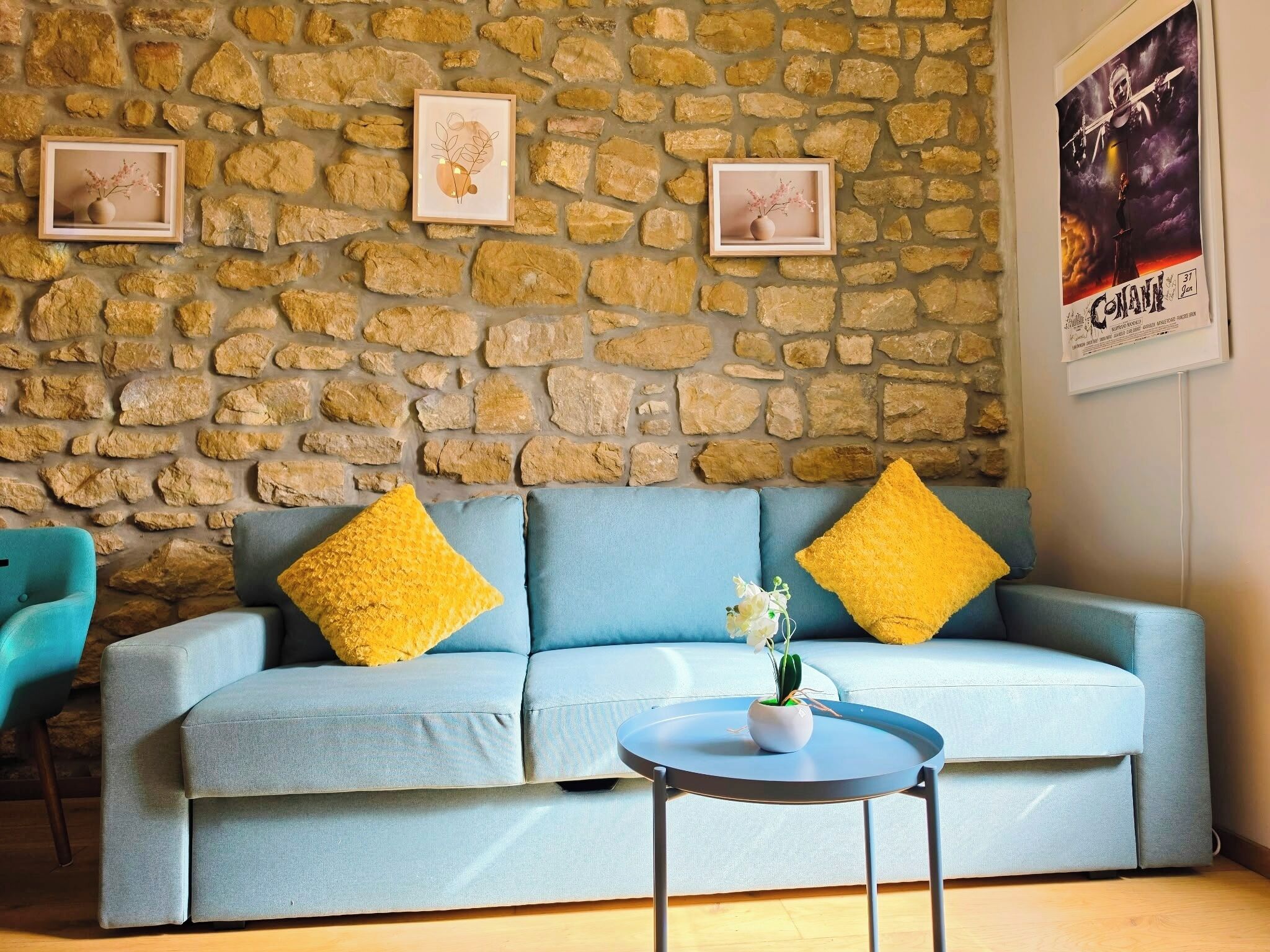 Ein Zimmer mit einer Steinsäule, einem hellblauen Sofa mit gelben Kissen, einem kleinen runden Tisch und zwei gerahmten Bildern.