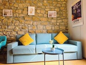 Ein Zimmer mit einer Steinsäule, einem hellblauen Sofa mit gelben Kissen, einem kleinen runden Tisch und zwei gerahmten Bildern.