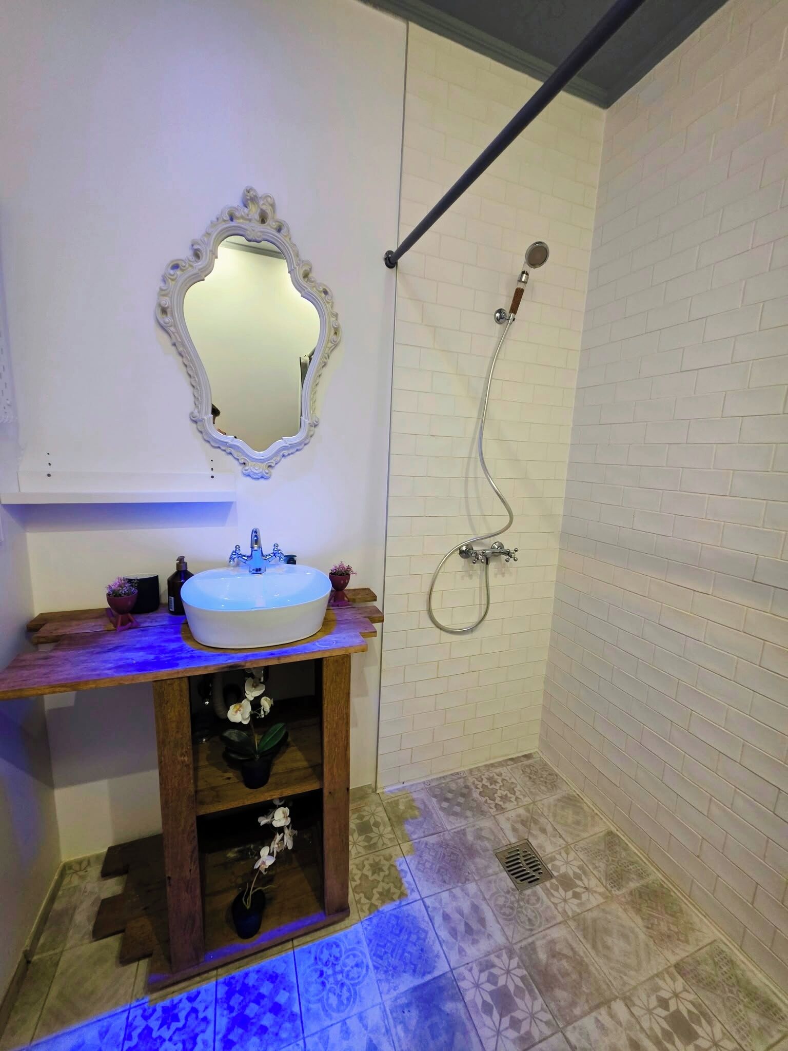 Casa de banho com lavatório branco, espelho e chuveiro.