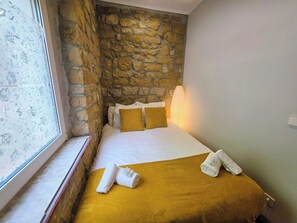 Ein Hotelzimmer mit Steinwand, einem Bett mit weißen Leinentüchern, einer gelben Tagesdecke und zwei Handtüchern auf dem Bett.