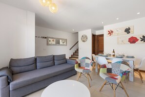 A modern living room with a grey sofa, a dining area with a table set for four, and a staircase leading to another level. - Home2Book Bellavista Puerto Calero Pool & BBQ (Puerto Calero)