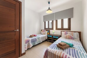 A bedroom with two beds, a wooden wardrobe, a desk, and a hanging light fixture. - Home2Book Bellavista Puerto Calero Pool & BBQ (Puerto Calero)