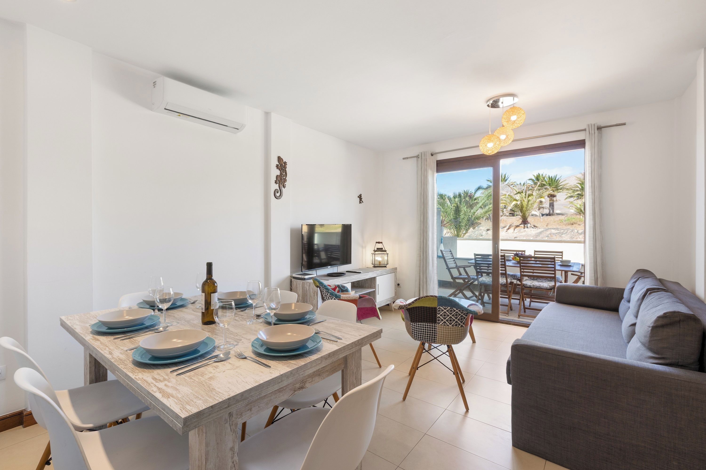 A modern living space with a dining area, a sofa, and a balcony with a view of palm trees.