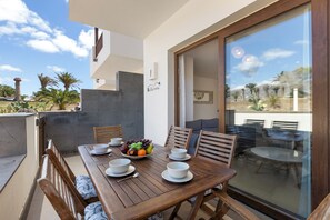 A dining area with a wooden table set for four, a bowl of fruit, and a view of the surrounding landscape. - Home2Book Bellavista Puerto Calero Pool & BBQ (Puerto Calero)