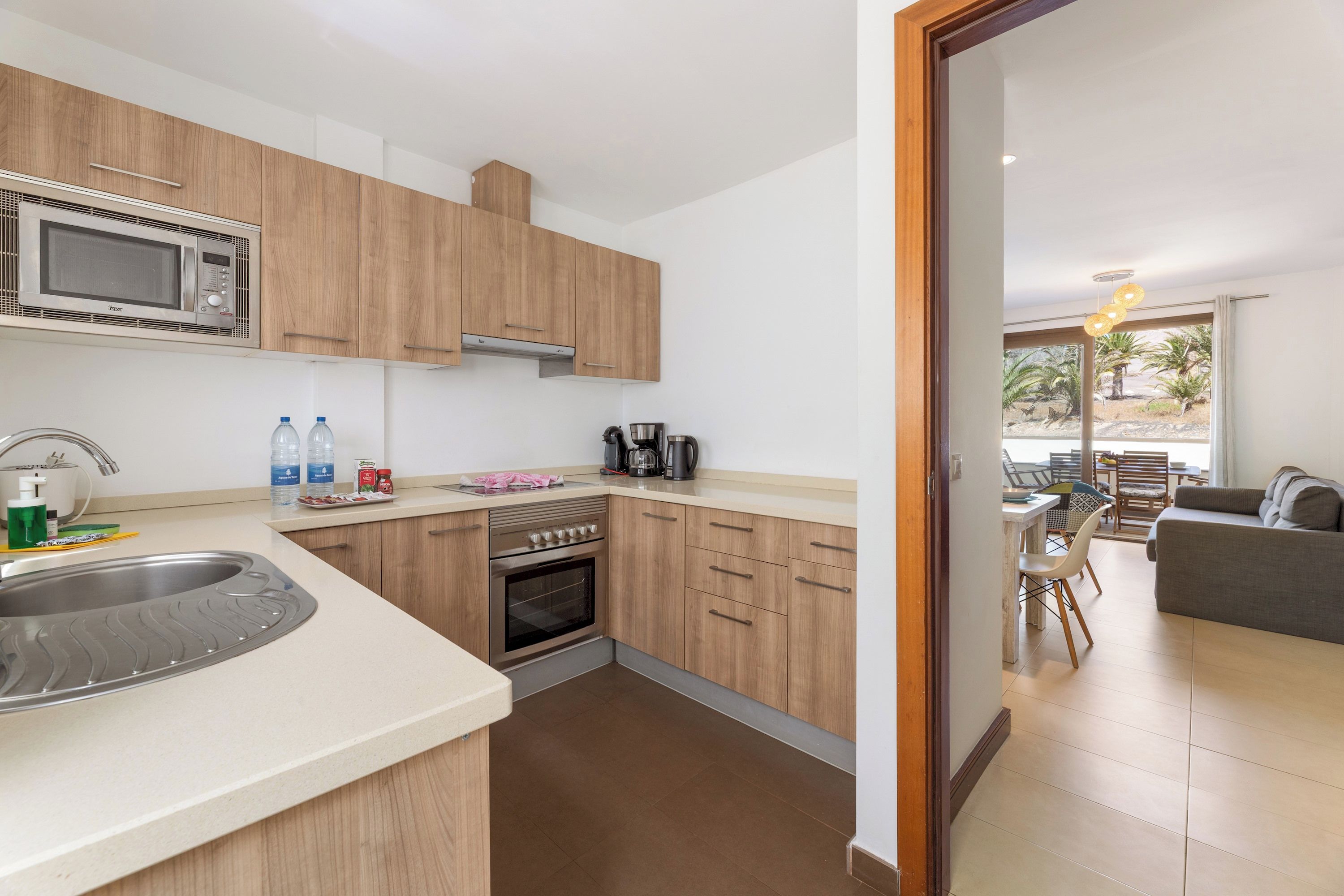 A modern kitchen with a microwave, oven, and sink. There is a dining area with a table and chairs visible through an open door.
