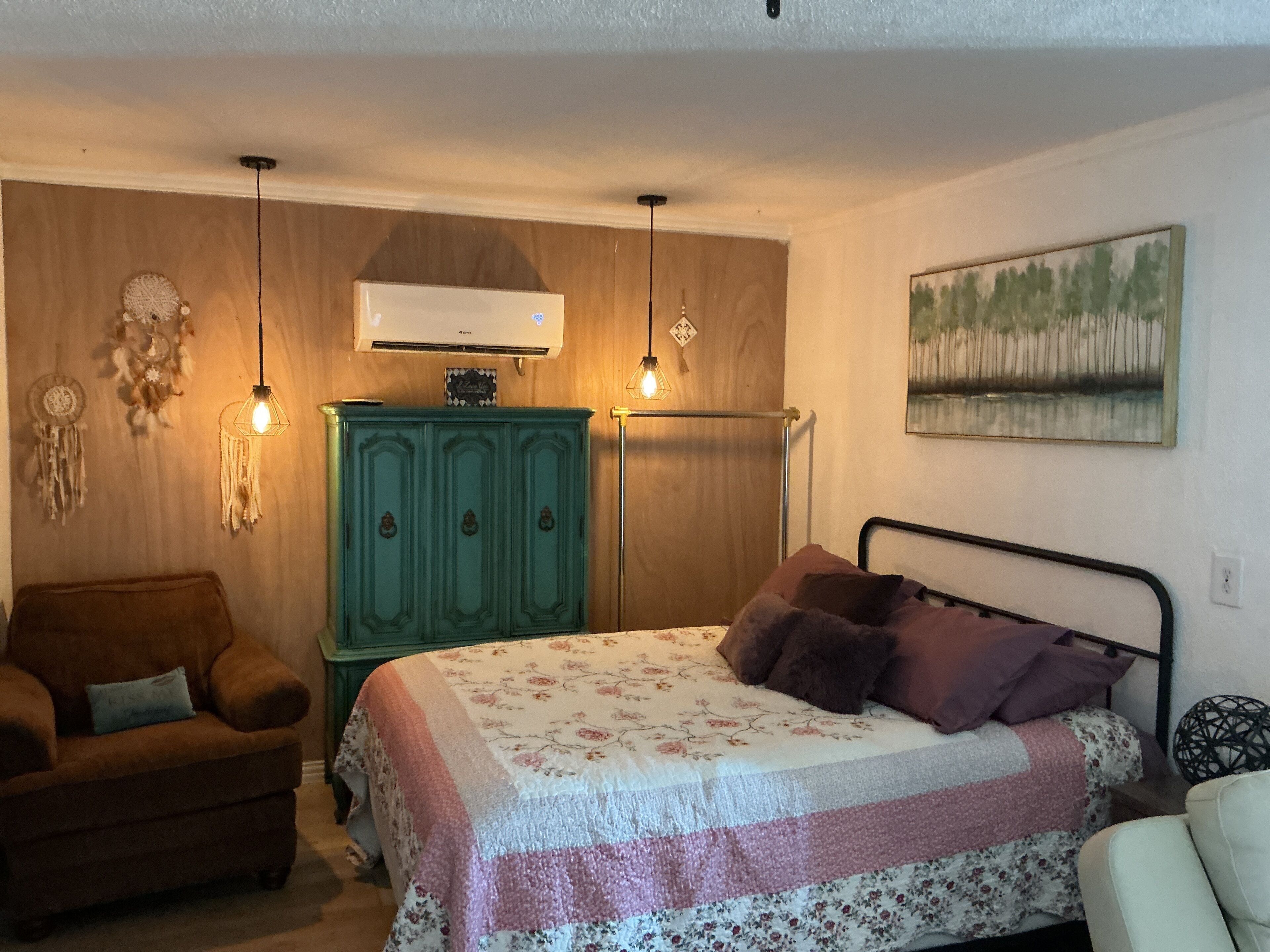 Une chambre à coucher avec un lit, une commode verte, une chaise et un climatiseur fixé au mur.