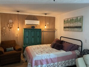 Ein Schlafzimmer mit einem Bett, einem grünen Schminktisch, einem Sessel und einer Wand-Klimaanlage.