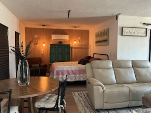 A cozy living room with a sofa, a dining table with chairs, a green cabinet, and a bed with a floral bedspread. - Wonderful studio with a couch like butter and jetted bathtub! (Fort Worth)