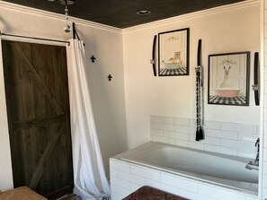 A bathroom with a white bathtub, a wooden door, and two framed pictures on the wall. - Wonderful studio with a couch like butter and jetted bathtub! (Fort Worth)