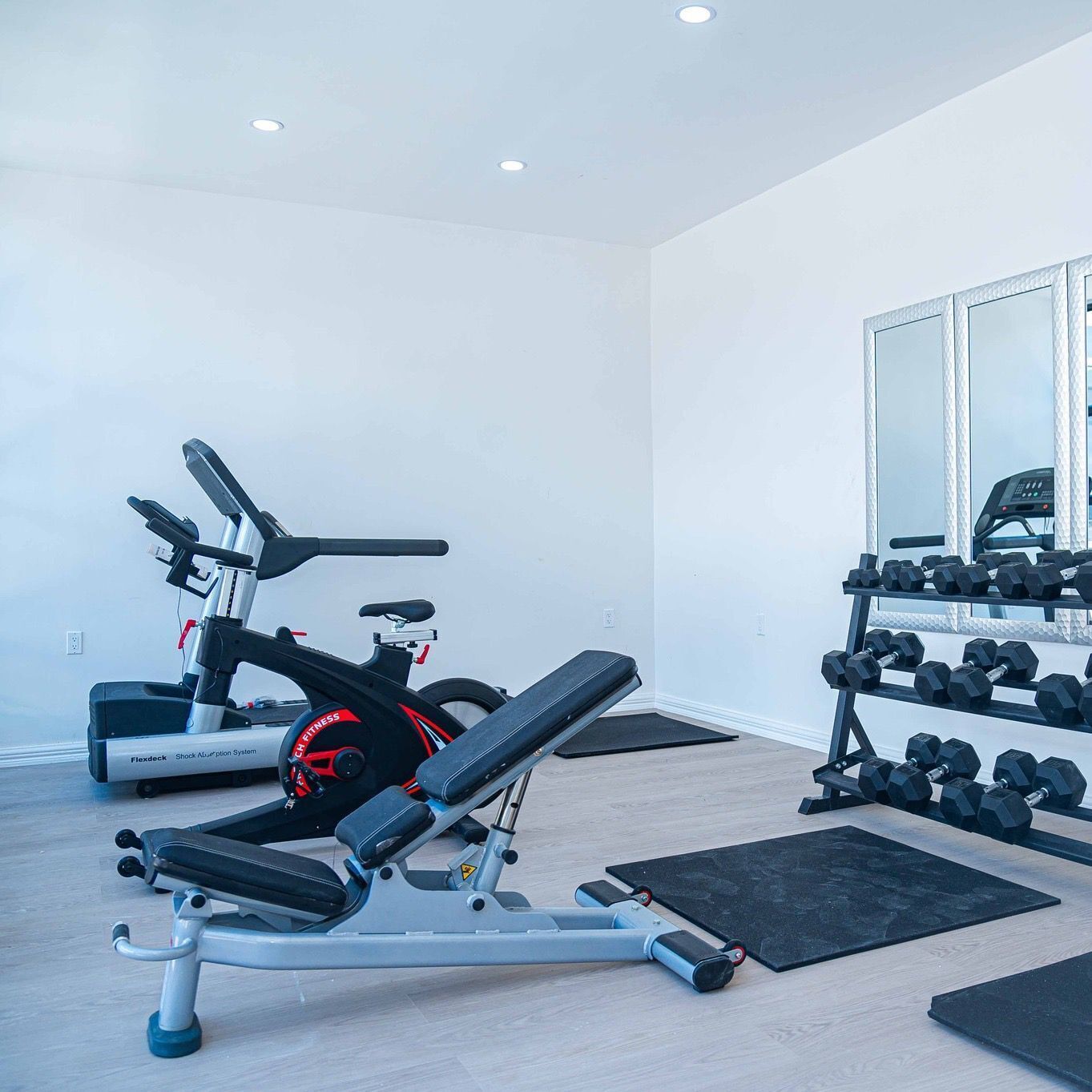 A home gym with a stationary bike, a bench press, and a rack of dumbbells.