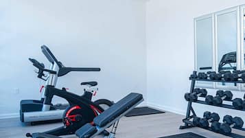 A home gym with a stationary bike, a bench press, and a rack of dumbbells.