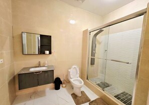 Un baño con inodoro, lavabo y cabina de ducha con mampara de vidrio.