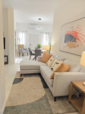 Un salon moderne avec un canapé d’angle, un coin repas et un grand tableau abstrait accroché au mur.