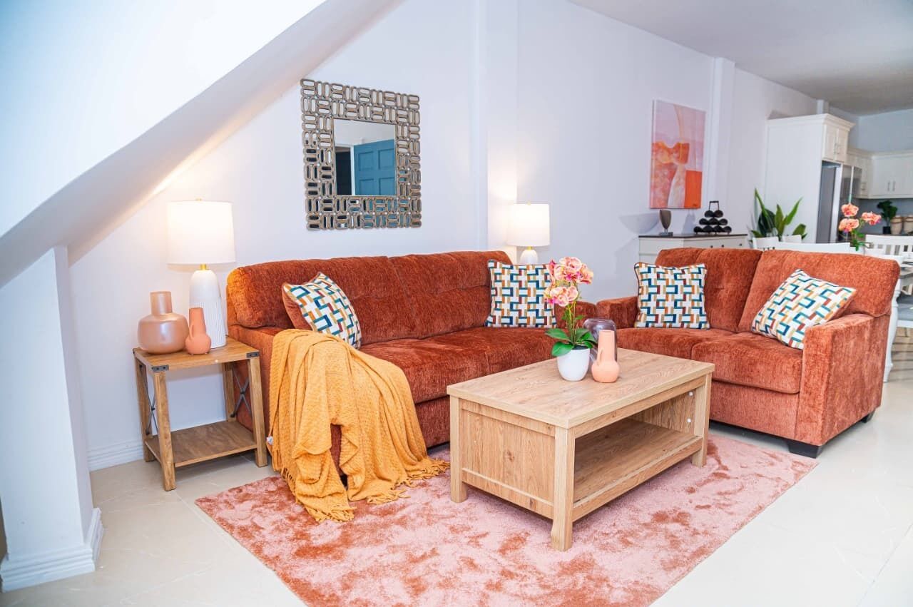 Uma sala de estar com sofá, duas mesas laterais, uma mesa de centro e um tapete.