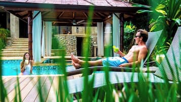 A pool area with a lounge chair, a person relaxing, and a woman in the water.