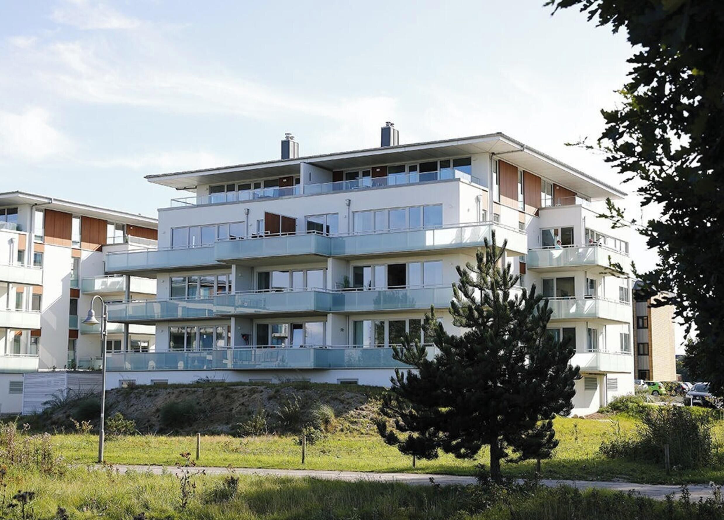 A multi-story residential building with balconies, a clear sky, and a tree in the foreground.