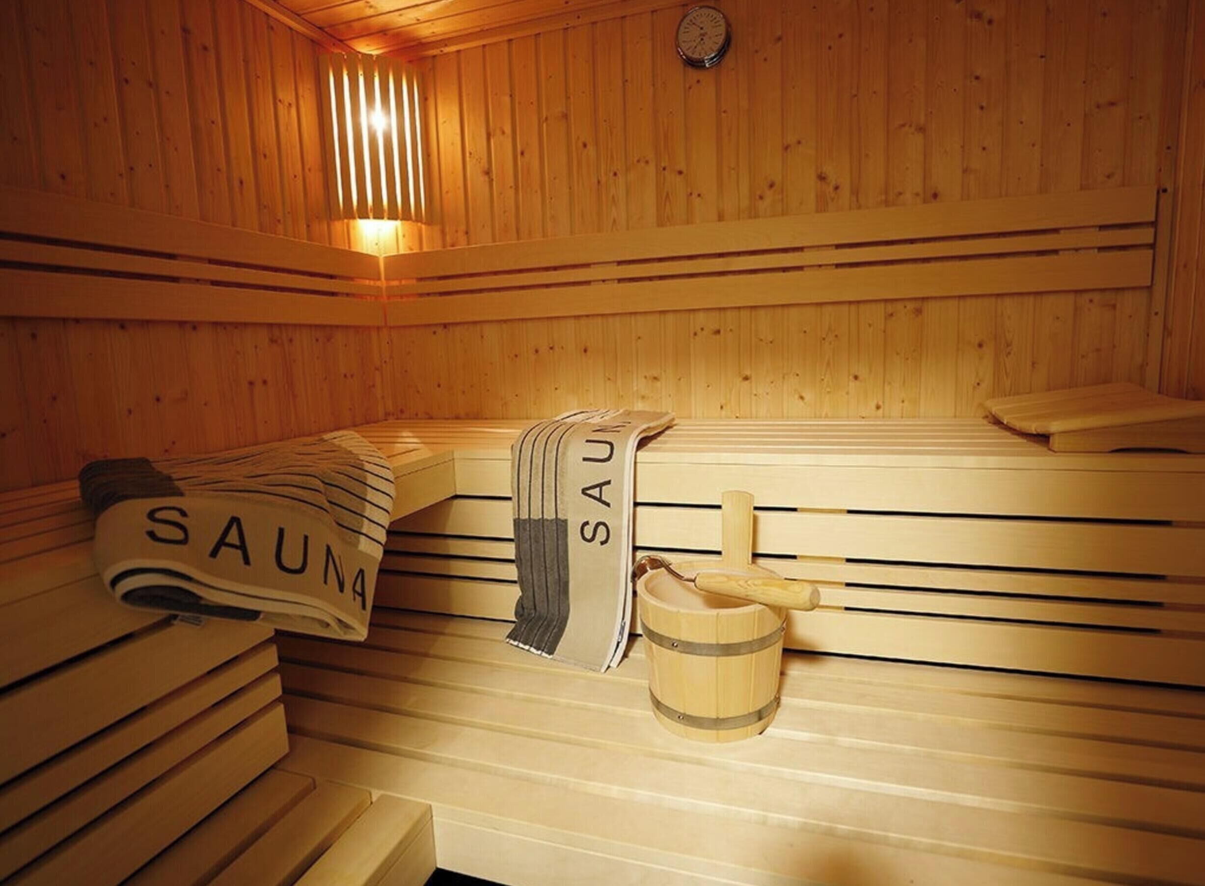 Een sauna met houten banken, handdoeken en een houten emmer.