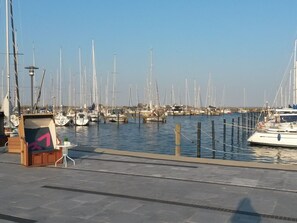Un port esportiu amb diverses embarcacions amarrades, una estructura de fusta amb un rètol, i un cel serè.