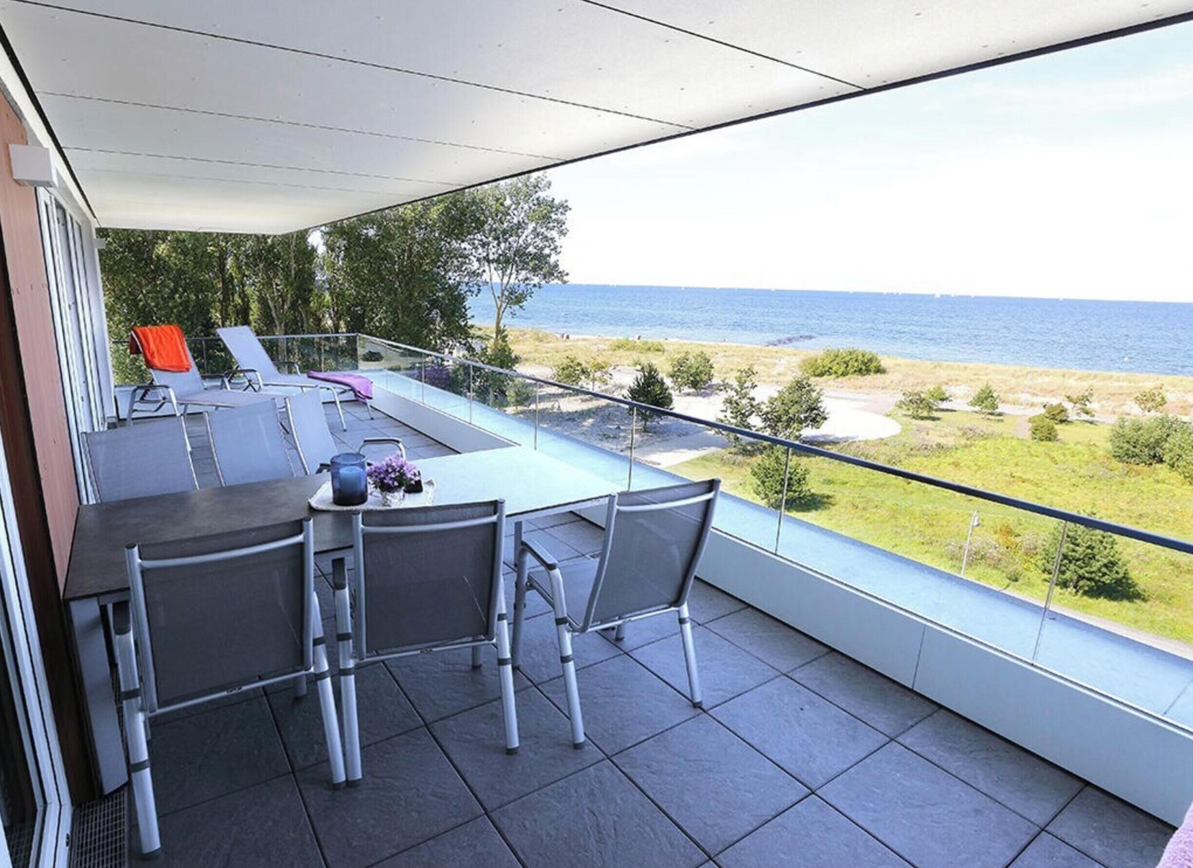 A balcony with a table, chairs, and a view of the sea.