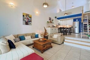A modern living room with a sofa, coffee table, and a kitchen area in the background. - Freebird by the beach (Cupecoy)