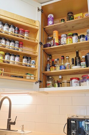 A kitchen with wooden shelves stocked with various spices and condiments. - Freebird by the beach (Cupecoy)