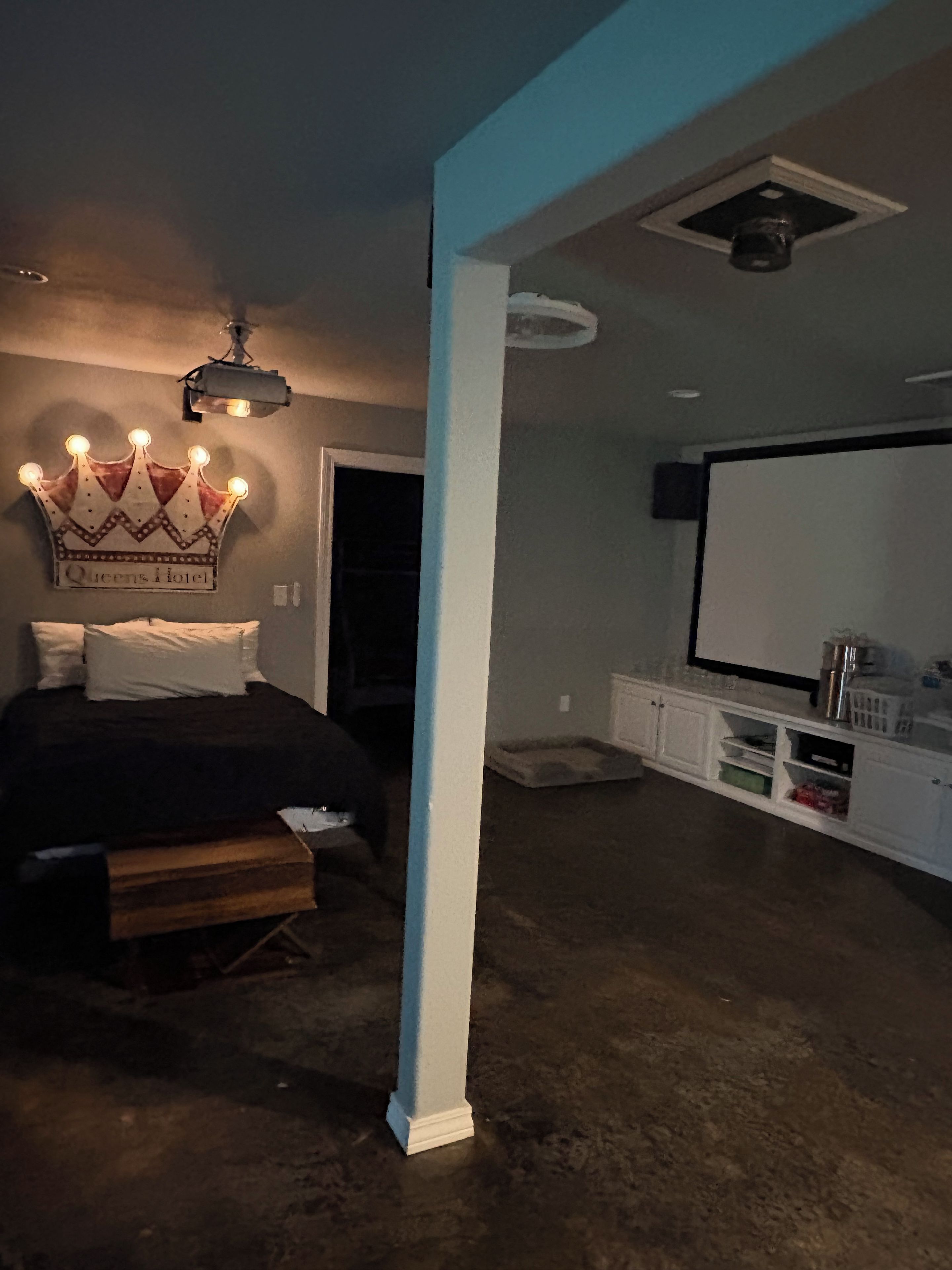 A bedroom with a bed, a crown-shaped light fixture, a white column, and a television on a stand.