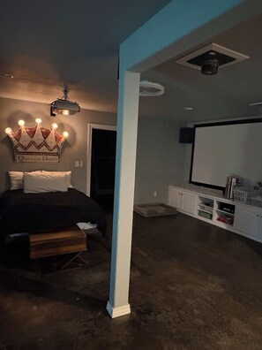 Quarto com cama, luminária em formato de coroa, coluna branca e televisão sobre suporte.