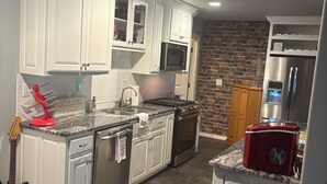 Una cocina moderna con armarios blancos, encimera de granito, electrodomésticos de acero inoxidable y una pared decorativa de ladrillo.
