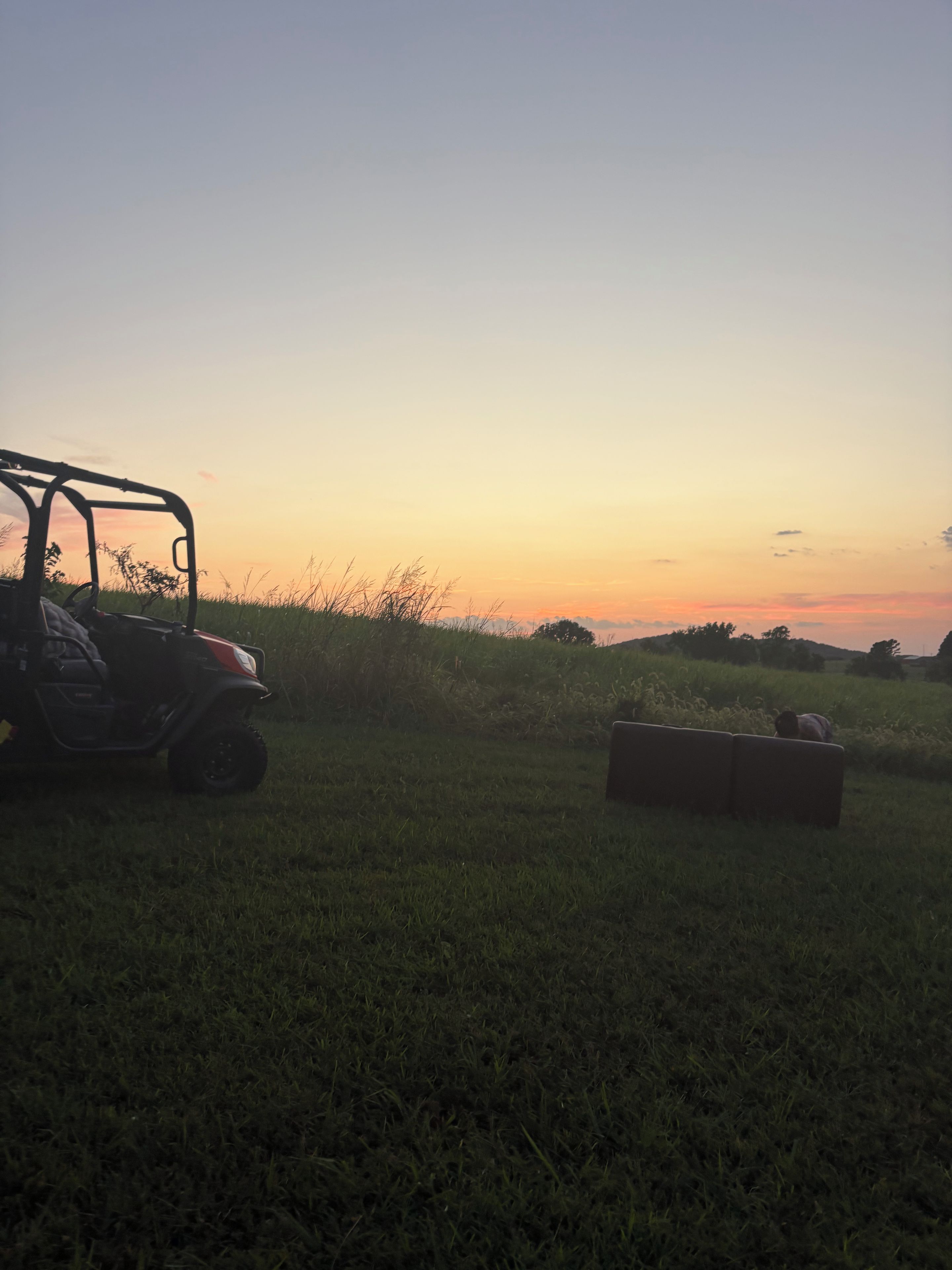 A vehicle parked in a grassy field with a sunset in the background.