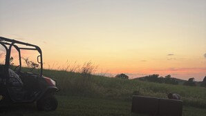 Un vehículo estacionado en un campo cubierto de hierba con un atardecer de fondo.