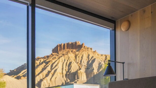 A room with a large window, a bed, and a view of a rocky landscape.