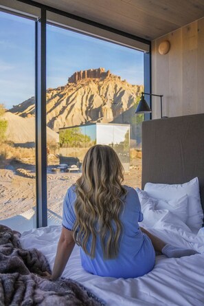 A room with a large window, a bed, and a view of a rocky landscape.