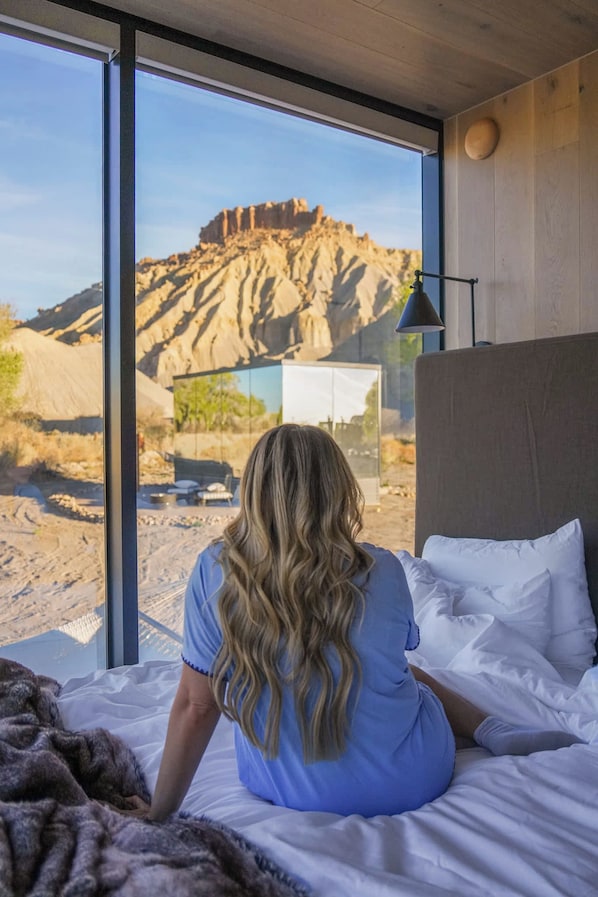 A room with a large window, a bed, and a view of a rocky landscape.