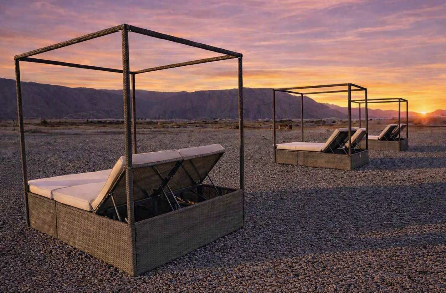 Outdoor lounge chairs with a metal frame and woven seat, set on a gravel surface with a mountainous backdrop.
